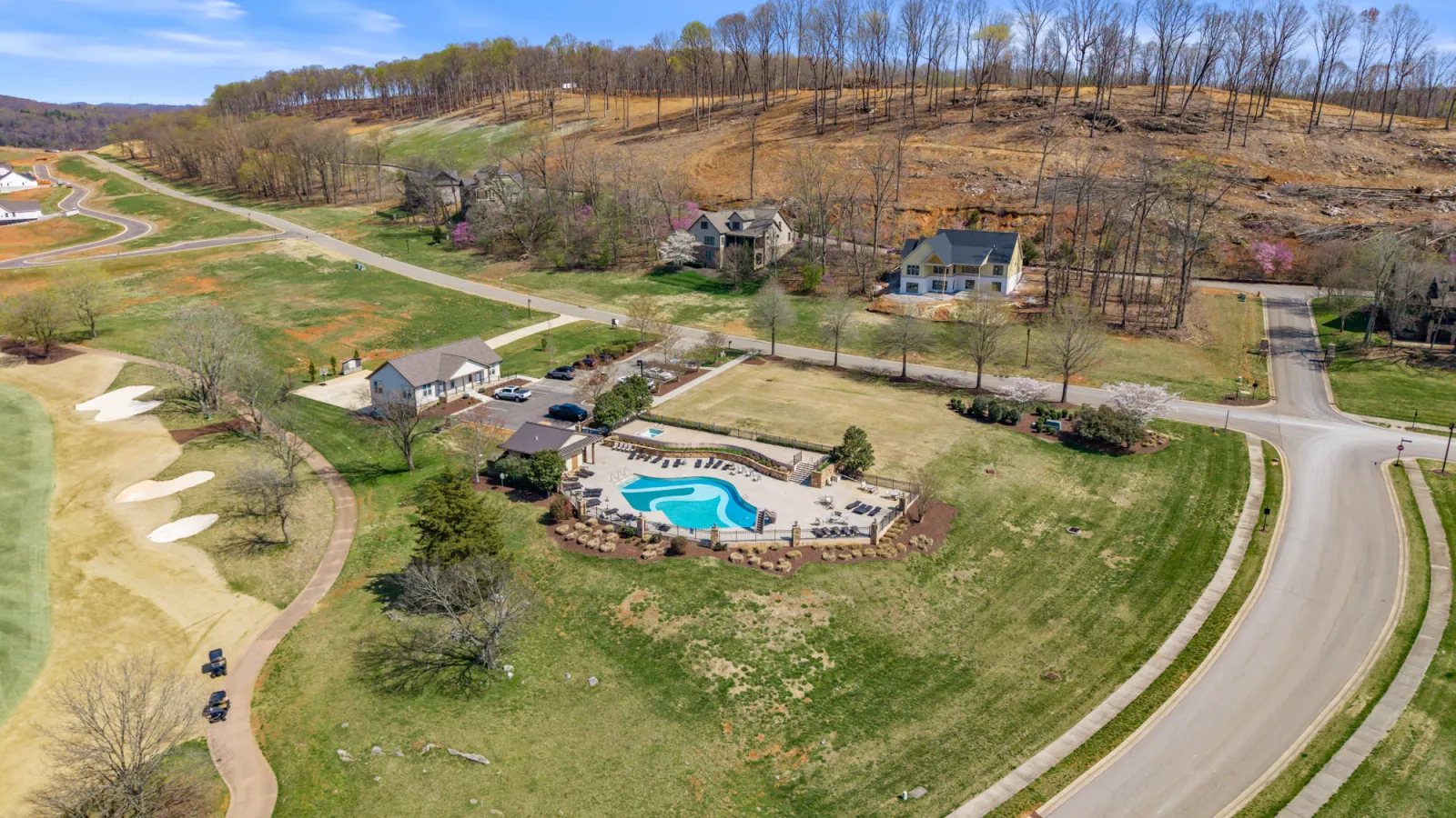 Aerial view of a rural subdivision with homes on large lots, winding roads, and wooded hills beyond