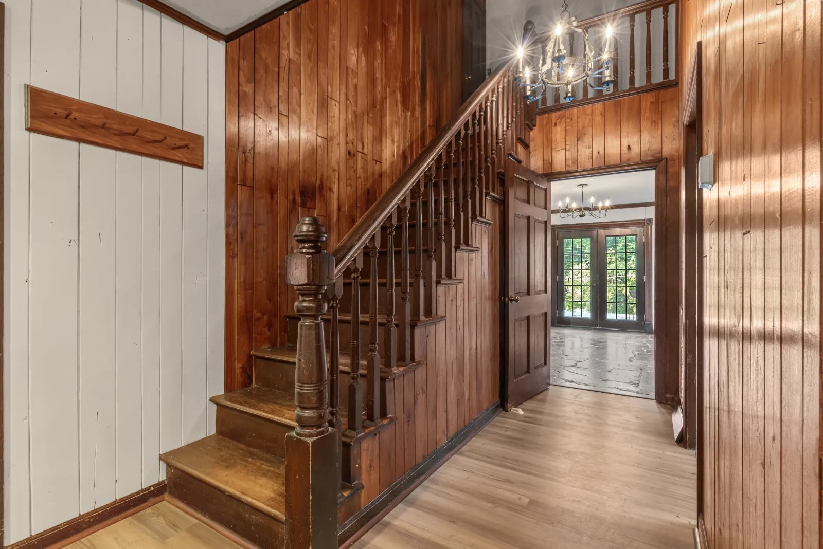 Entry hall with a dark wood-paneled staircase and a chandelier hanging over the landing