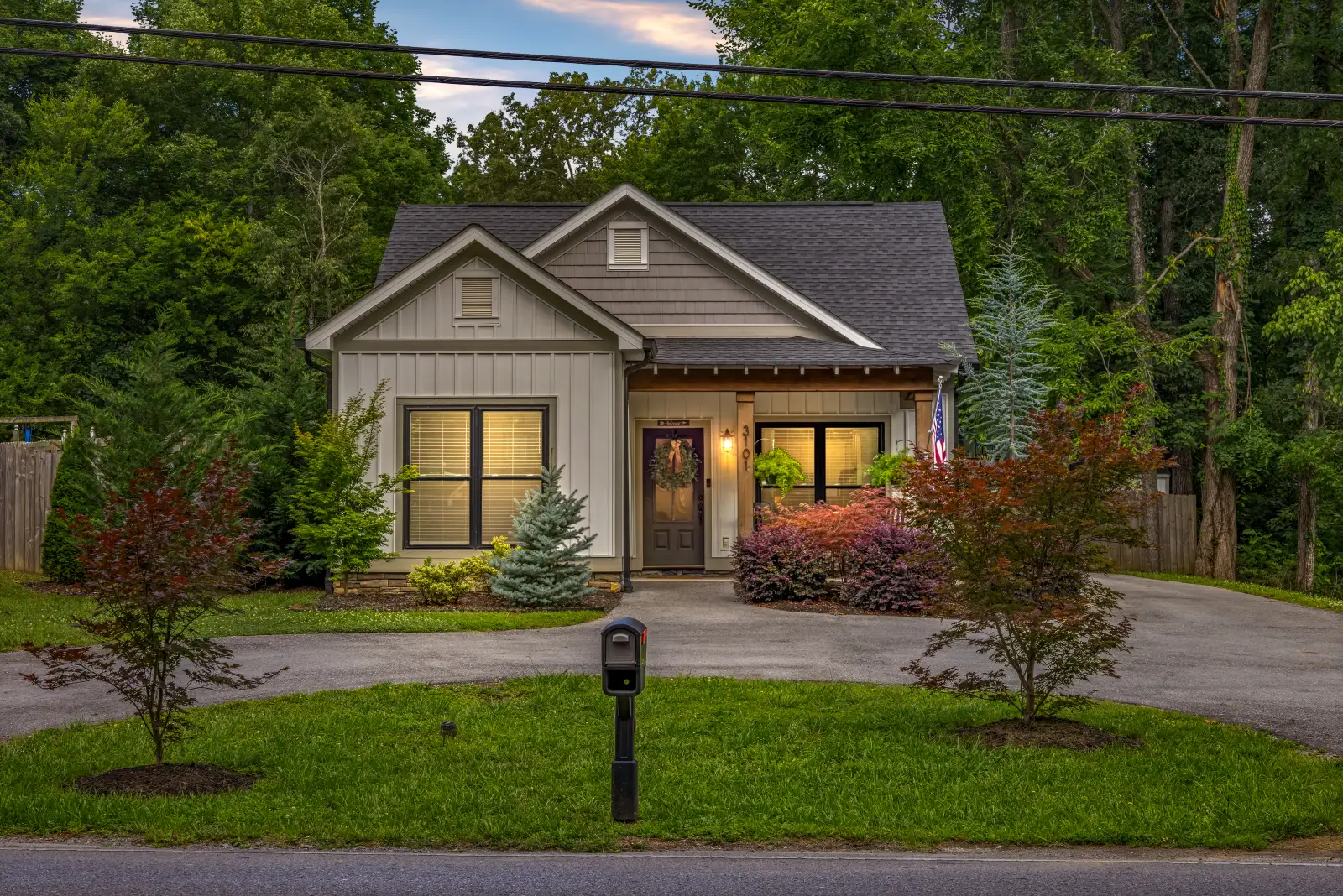 Craftsman-style home at dusk with the windows lit and a landscaped front lawn