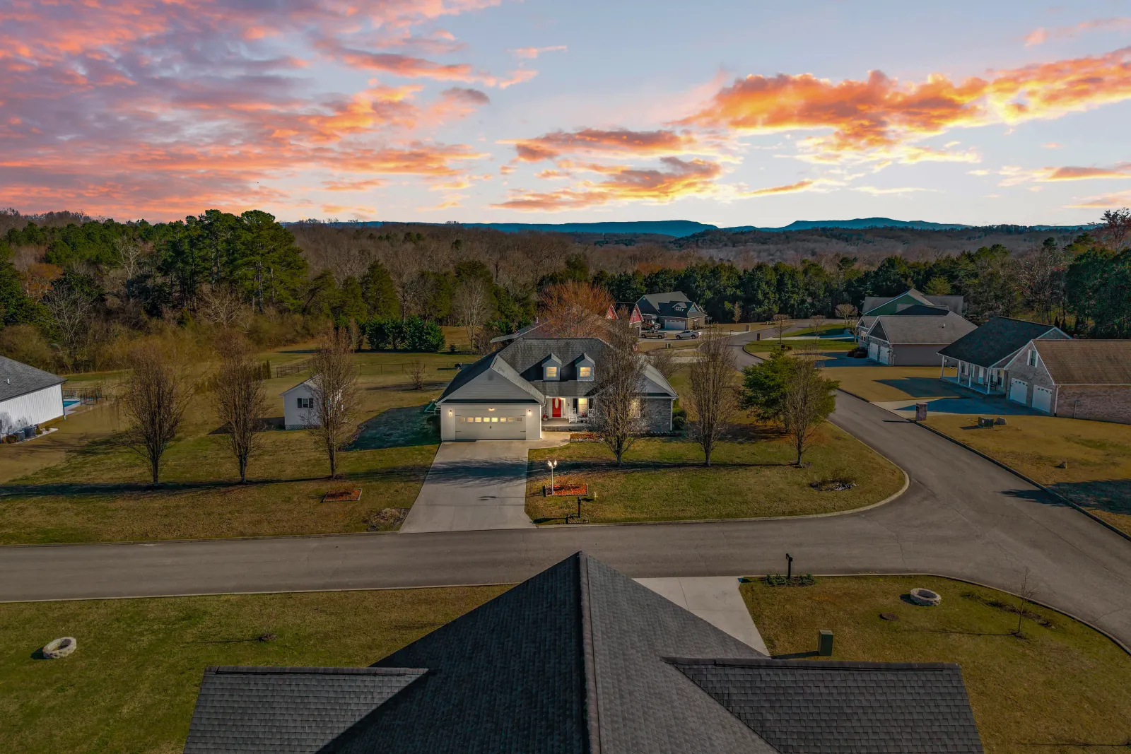 Drone photo at sunset over a residential neighborhood, rooftops in the foreground and wooded ridgelines on the horizon