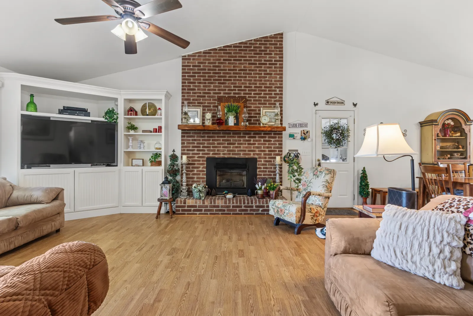 Living room with a brick fireplace flanked by white built-in shelves and hardwood floors