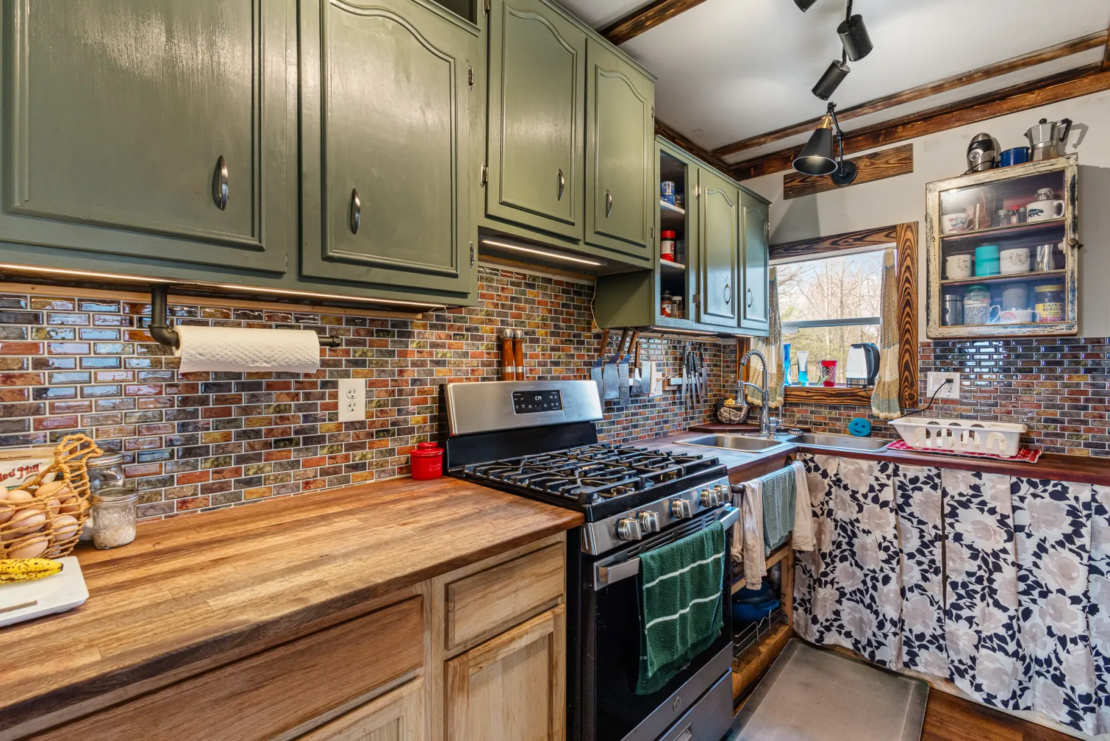 Farmhouse kitchen with sage green cabinets, exposed brick backsplash, butcher block counters, and a stainless gas range
