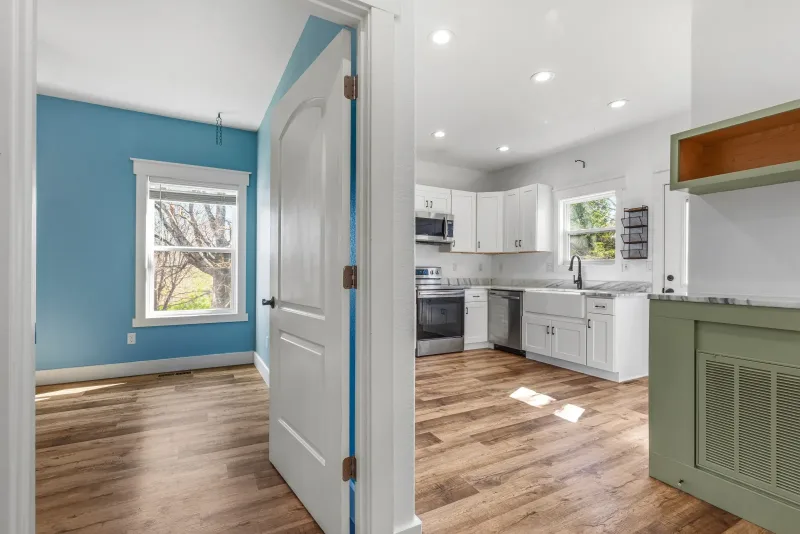 Open kitchen and hallway with white upper cabinets, sage lower cabinets, stainless appliances, and light wood flooring