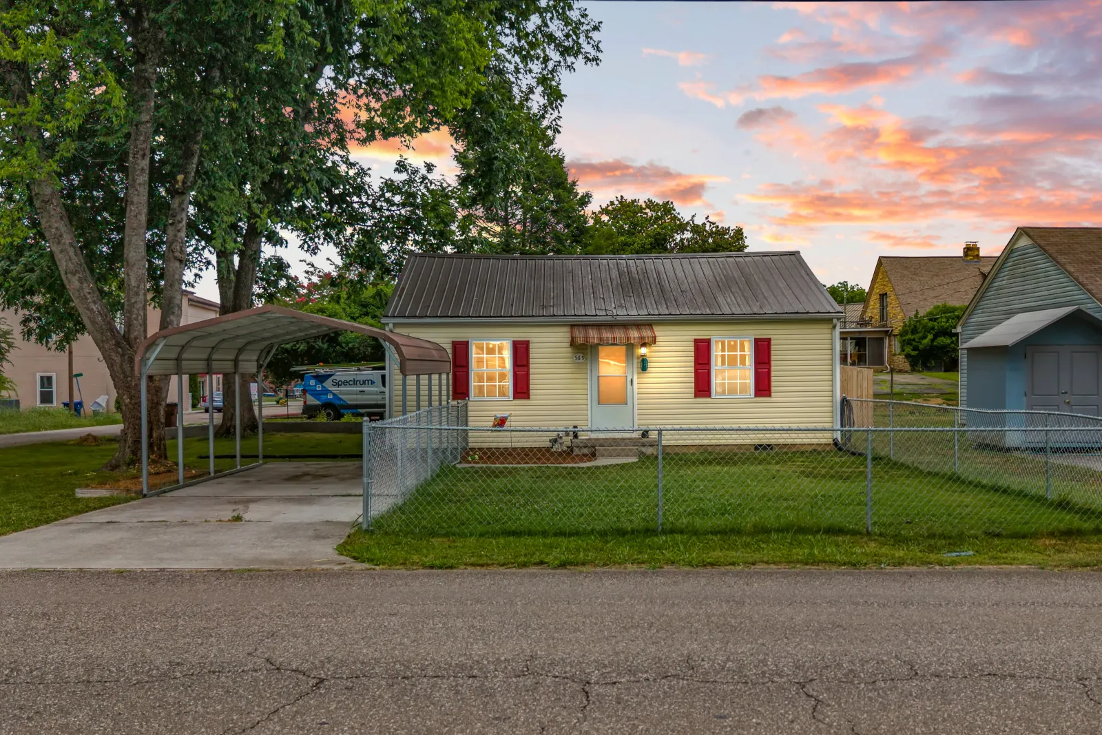 Small cottage with red shutters and a carport at twilight under an orange and pink sky