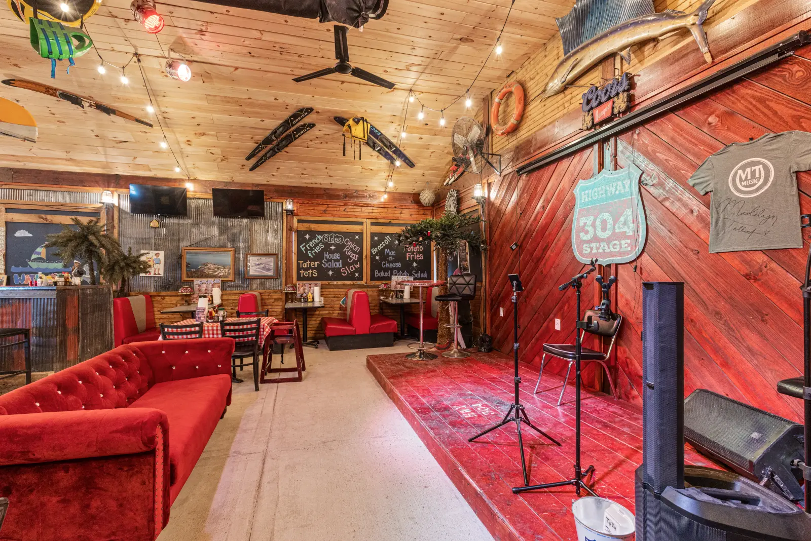 Knotty-pine music room with red velvet sofas, a stage rug, microphone stands, and string lights