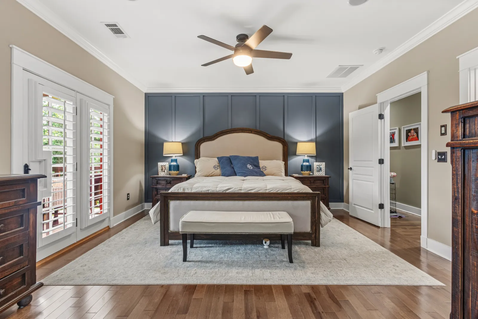 Primary bedroom with a navy accent wall, upholstered bed, ceiling fan, and plantation shutters