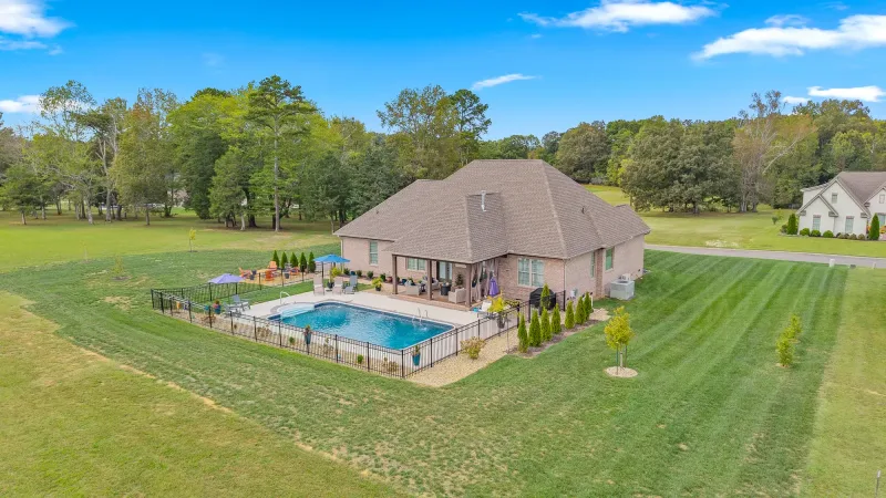 Aerial overview of a brick home with a fenced in-ground pool and a large landscaped lawn