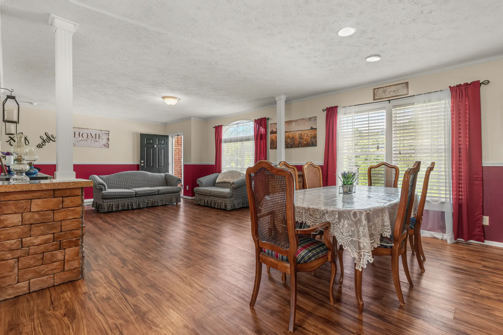Dining room with a lace-covered table, red drapes, and a column opening to the living room