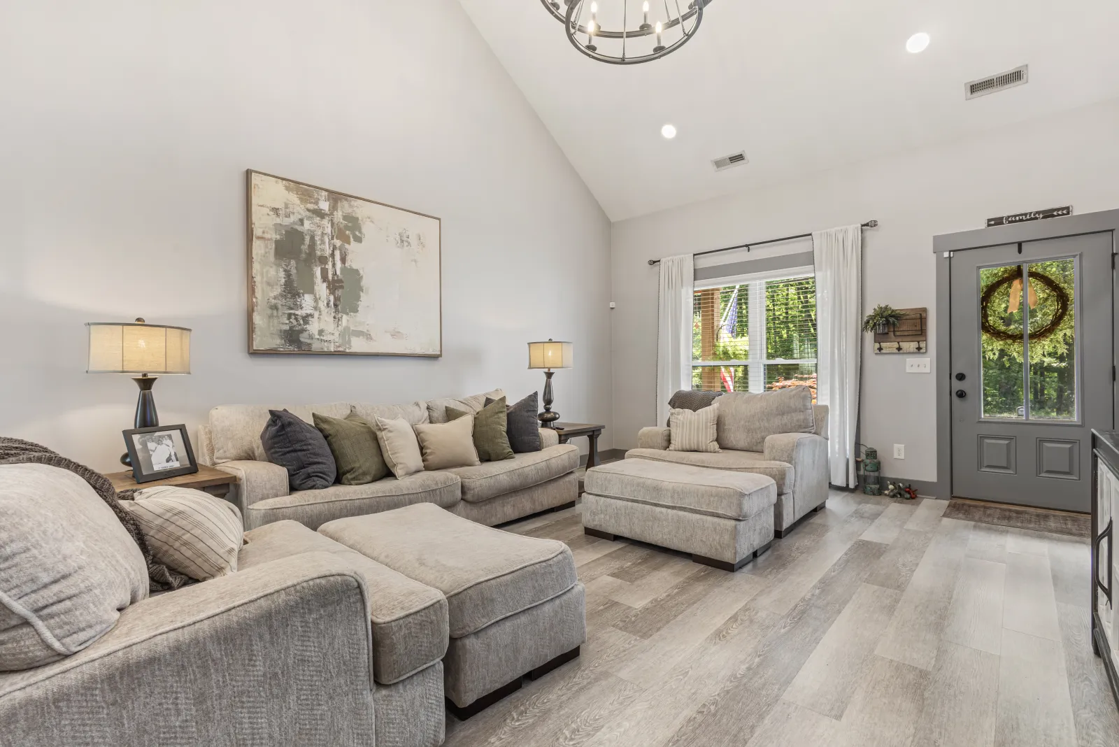 Living room with a vaulted ceiling, a gray sectional, and a front door hung with a wreath
