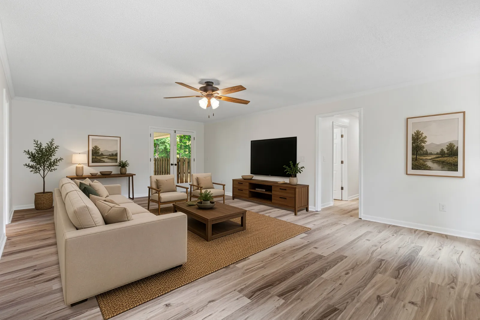 The same living room virtually staged with a cream sofa, two armchairs, a wood coffee table on a jute rug, a media console, and framed landscape art