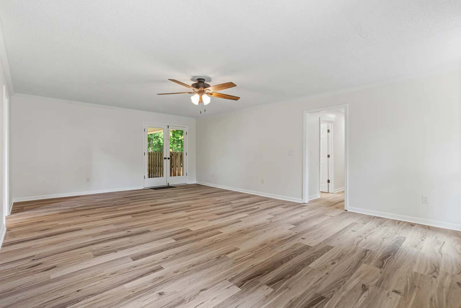 Empty living room with white walls, light wood floors, a ceiling fan, and French doors to the yard
