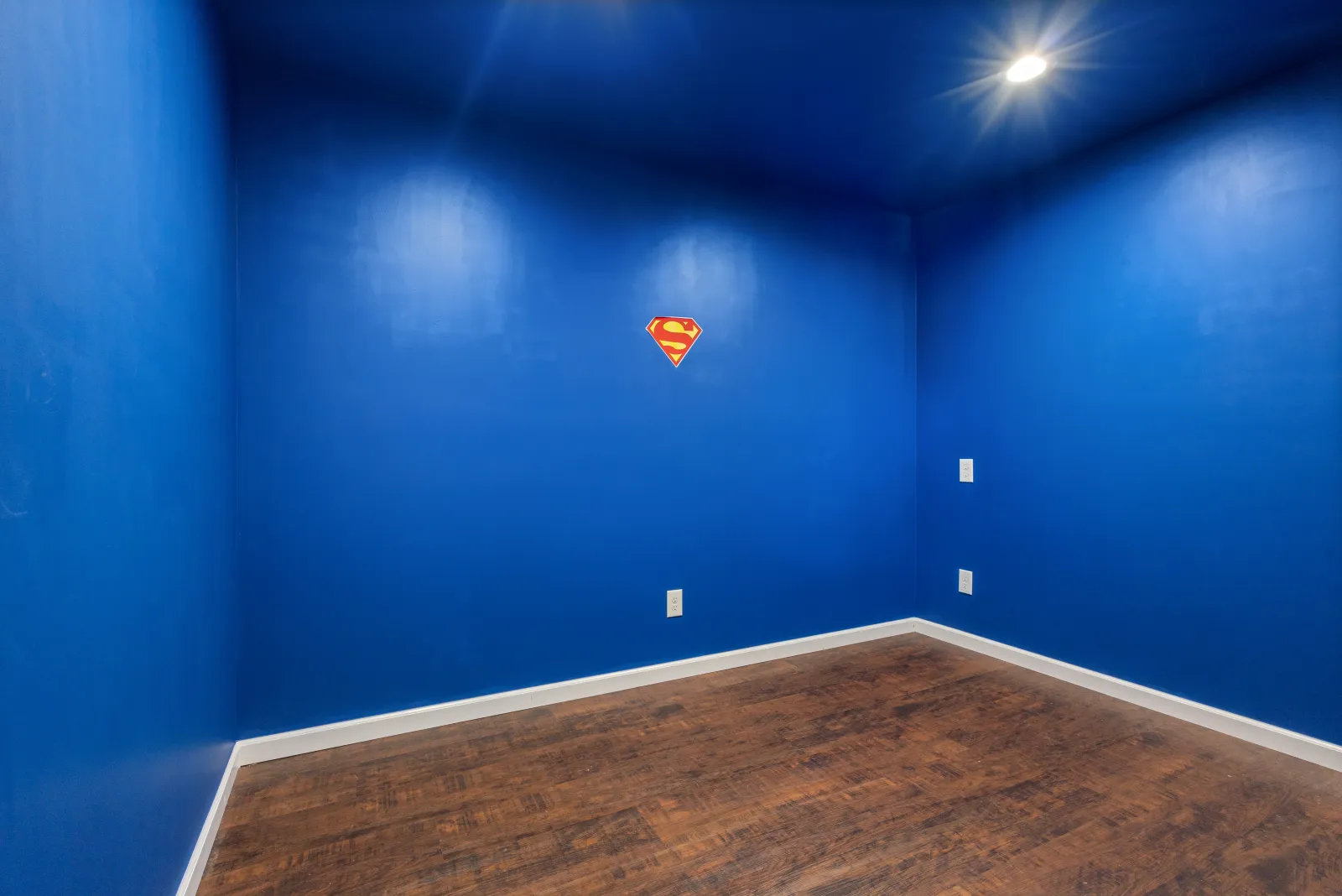 Empty bonus room with royal blue walls, dark wood floors, and a single recessed light